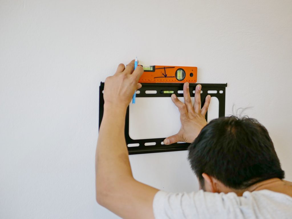 "Asian technician hands holding a TV wall mount against the wall while looking for the right angle to make a mark for a drilling for HDB interior design in singapore"