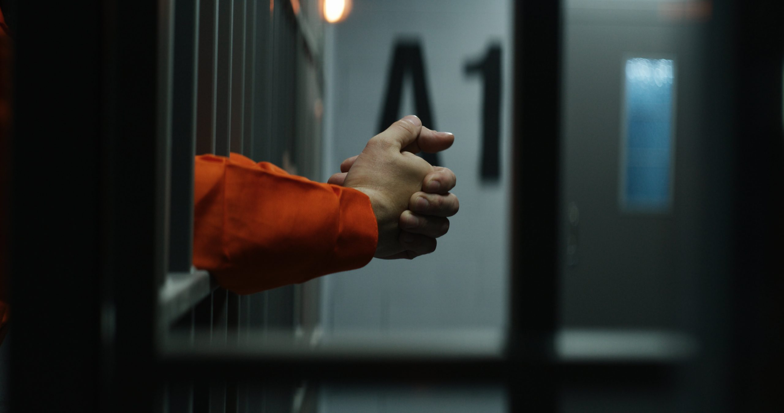 Hands clasped resting behind prison bars